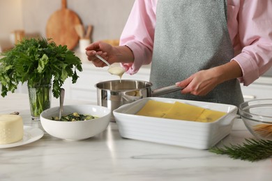 Photo of Woman making spinach lasagna at marble table indoors, closeup