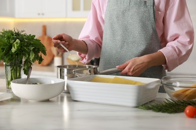 Photo of Woman making spinach lasagna at marble table indoors, closeup