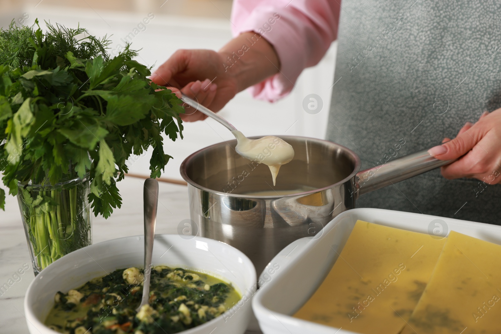 Photo of Woman making spinach lasagna at table indoors, closeup