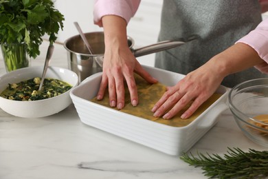 Photo of Woman making spinach lasagna at marble table indoors, closeup