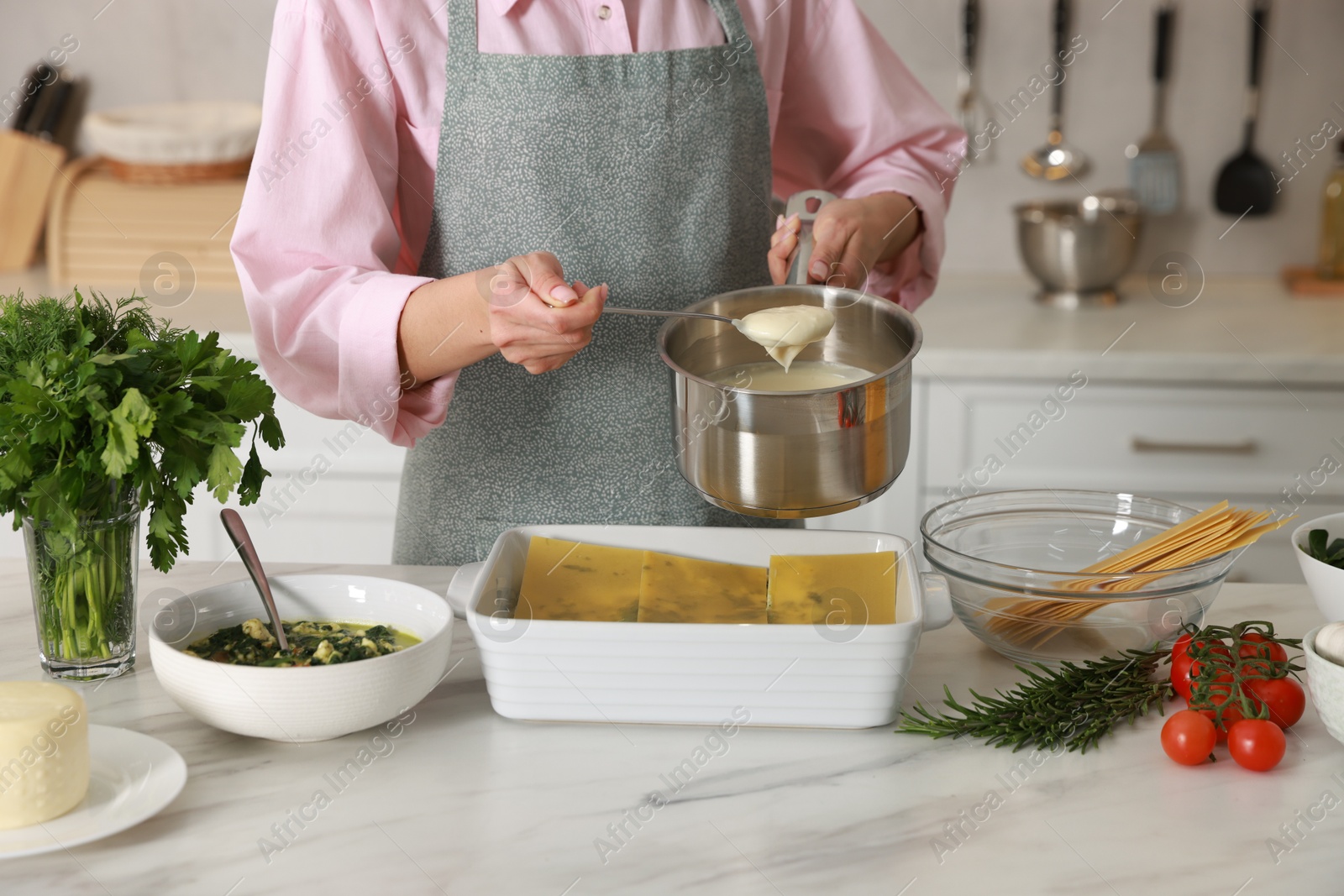 Photo of Woman making spinach lasagna at marble table in kitchen, closeup