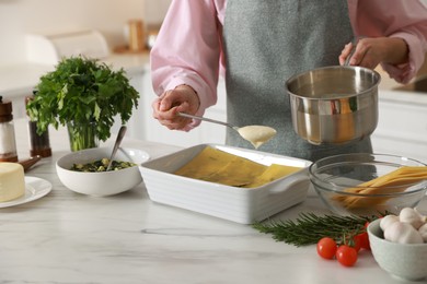 Photo of Woman spreading bechamel sauce onto spinach lasagna at marble table indoors, closeup