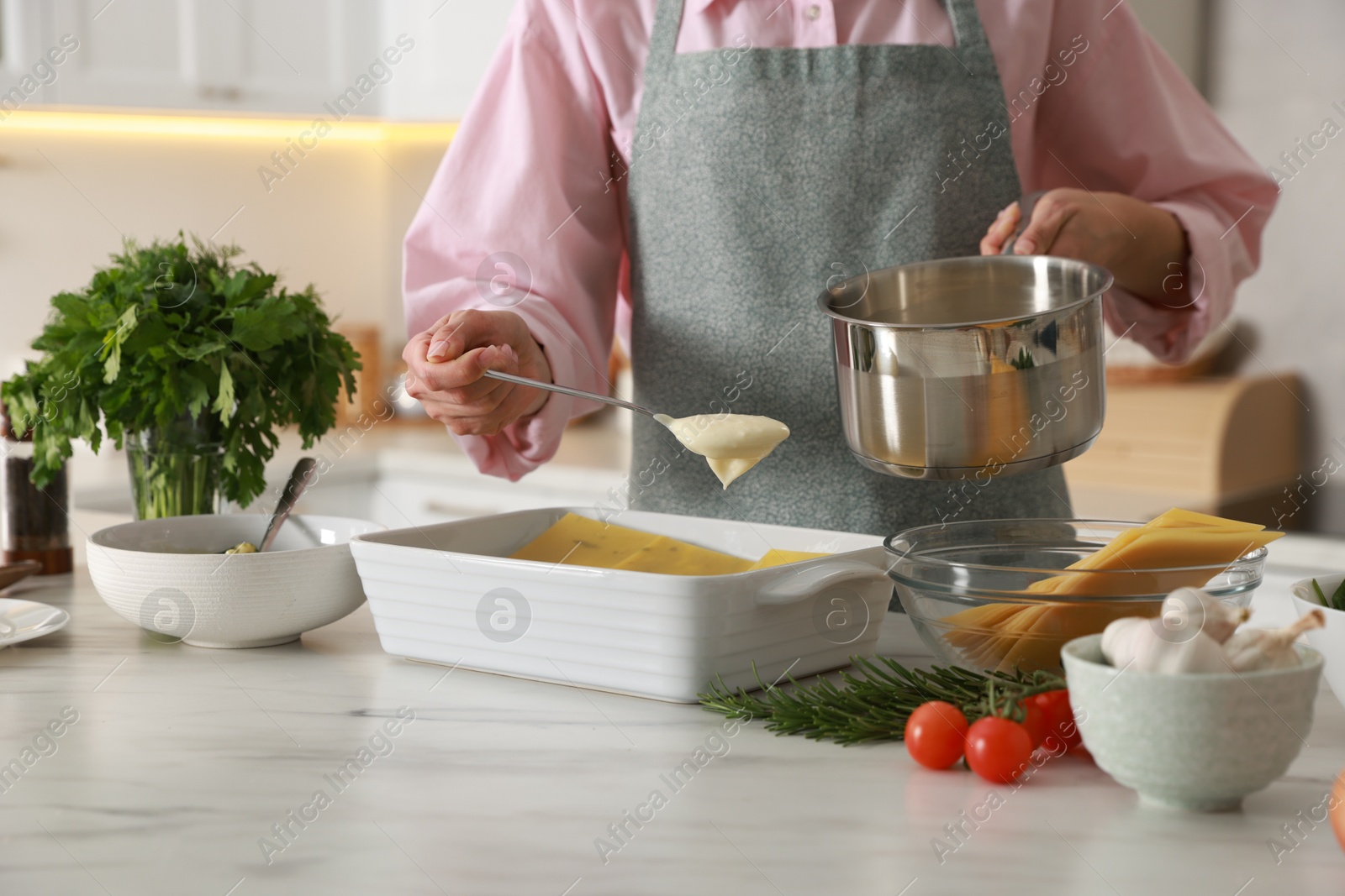 Photo of Woman spreading bechamel sauce onto spinach lasagna at marble table indoors, closeup