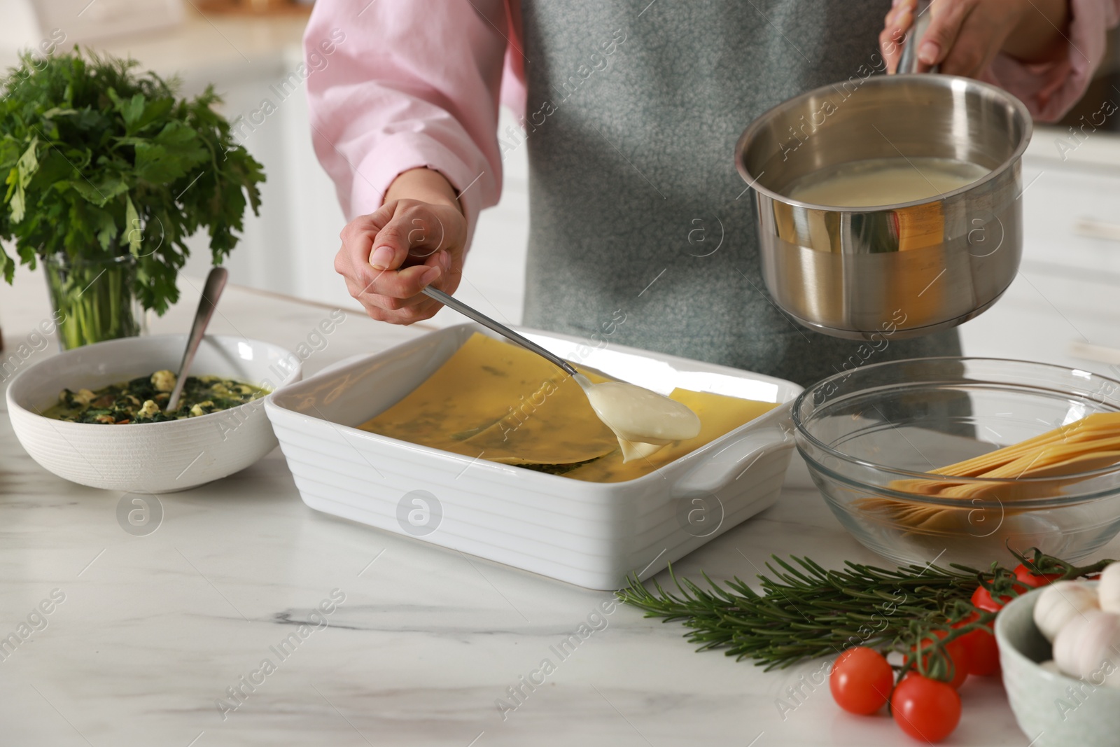 Photo of Woman spreading bechamel sauce onto spinach lasagna at marble table indoors, closeup