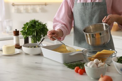 Photo of Woman spreading bechamel sauce onto spinach lasagna at marble table indoors, closeup