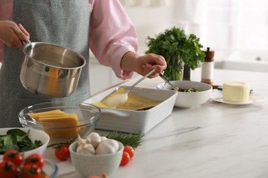 Photo of Woman spreading bechamel sauce onto spinach lasagna at marble table indoors, closeup