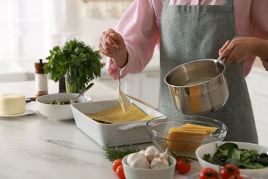 Photo of Woman spreading bechamel sauce onto spinach lasagna at marble table indoors, closeup