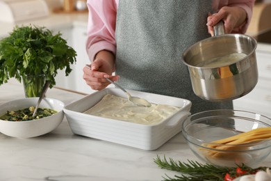 Photo of Woman spreading bechamel sauce onto spinach lasagna at marble table indoors, closeup