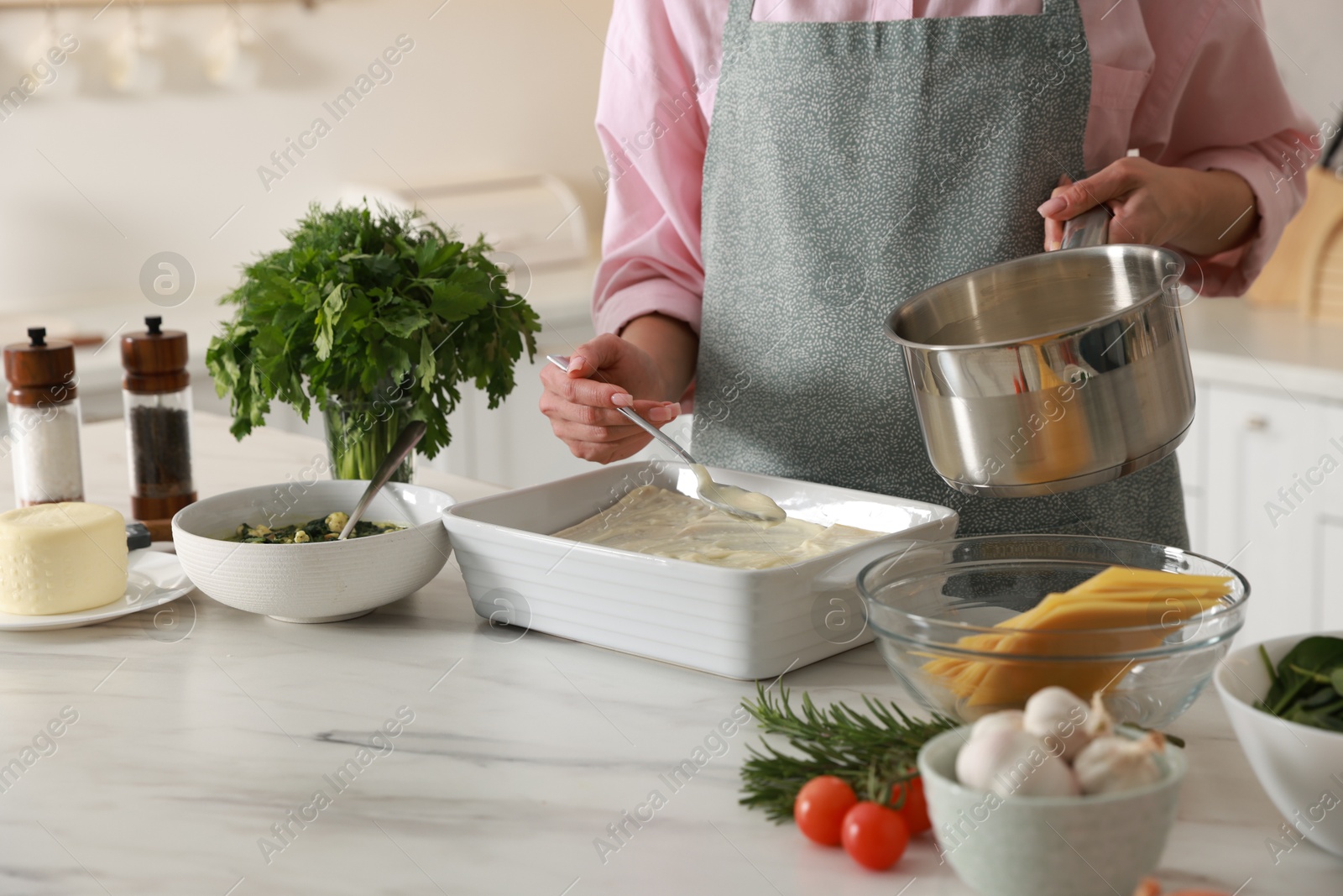 Photo of Woman spreading bechamel sauce onto spinach lasagna at marble table indoors, closeup