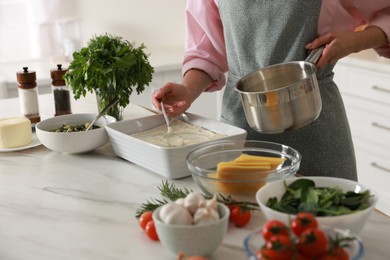 Photo of Woman spreading bechamel sauce onto spinach lasagna at marble table indoors, closeup