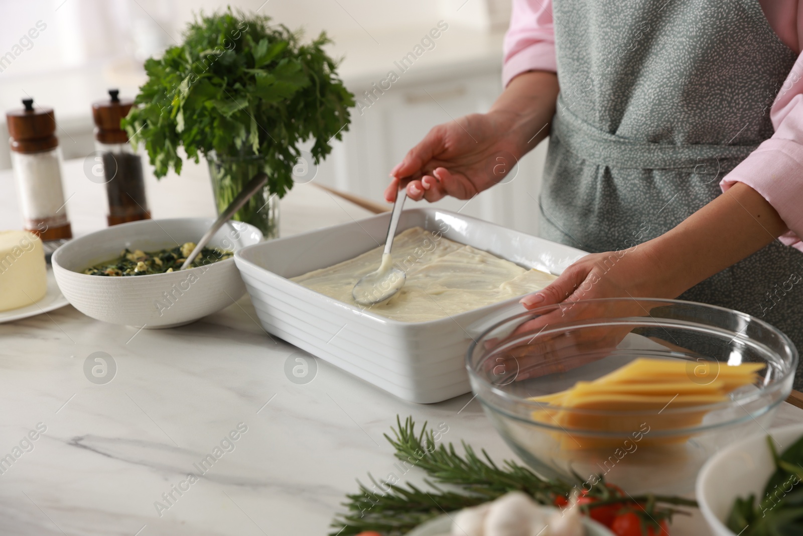 Photo of Woman spreading bechamel sauce onto spinach lasagna at marble table indoors, closeup