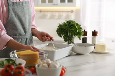 Photo of Woman spreading bechamel sauce onto spinach lasagna at marble table indoors, closeup