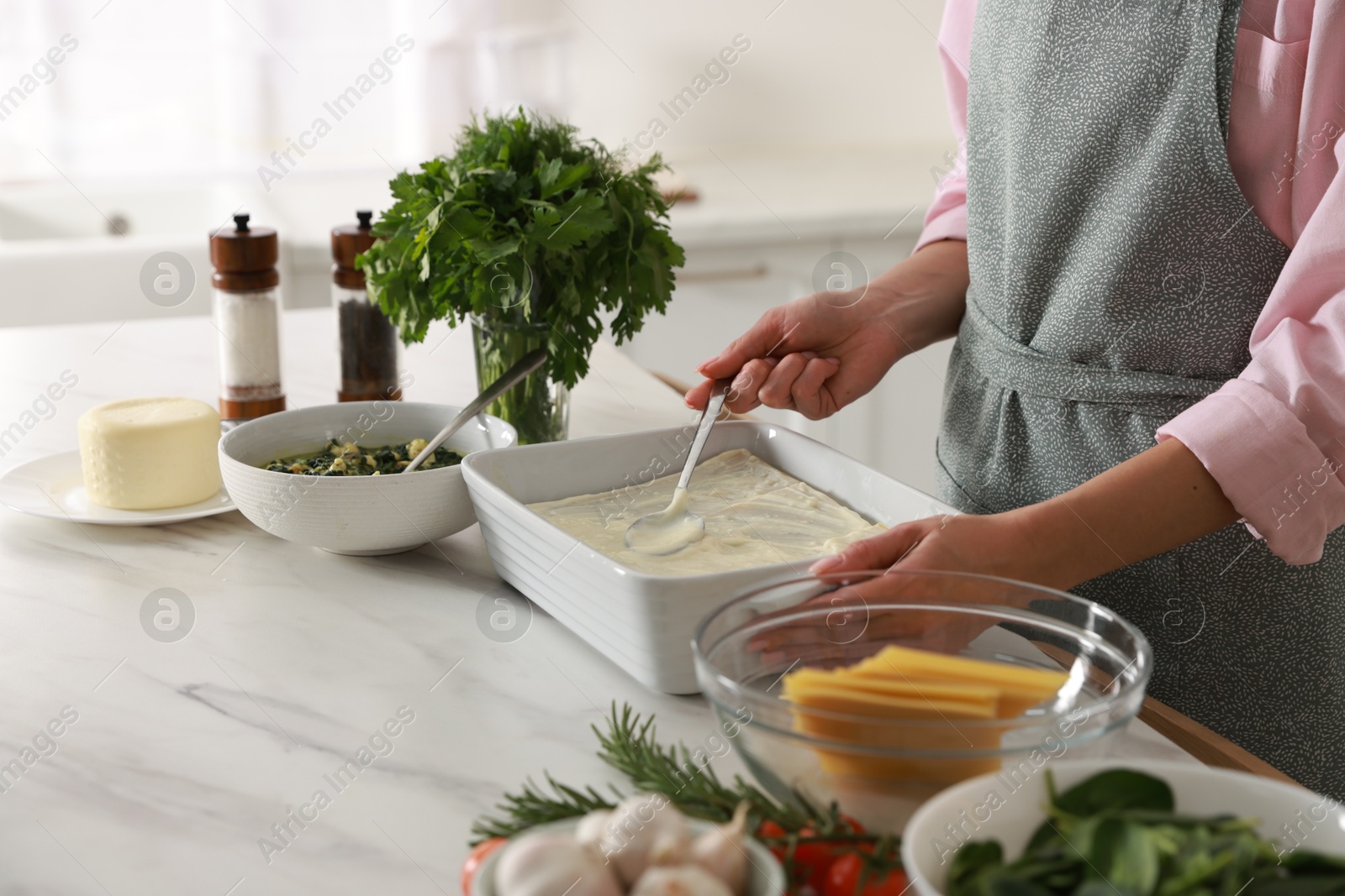 Photo of Woman spreading bechamel sauce onto spinach lasagna at marble table indoors, closeup