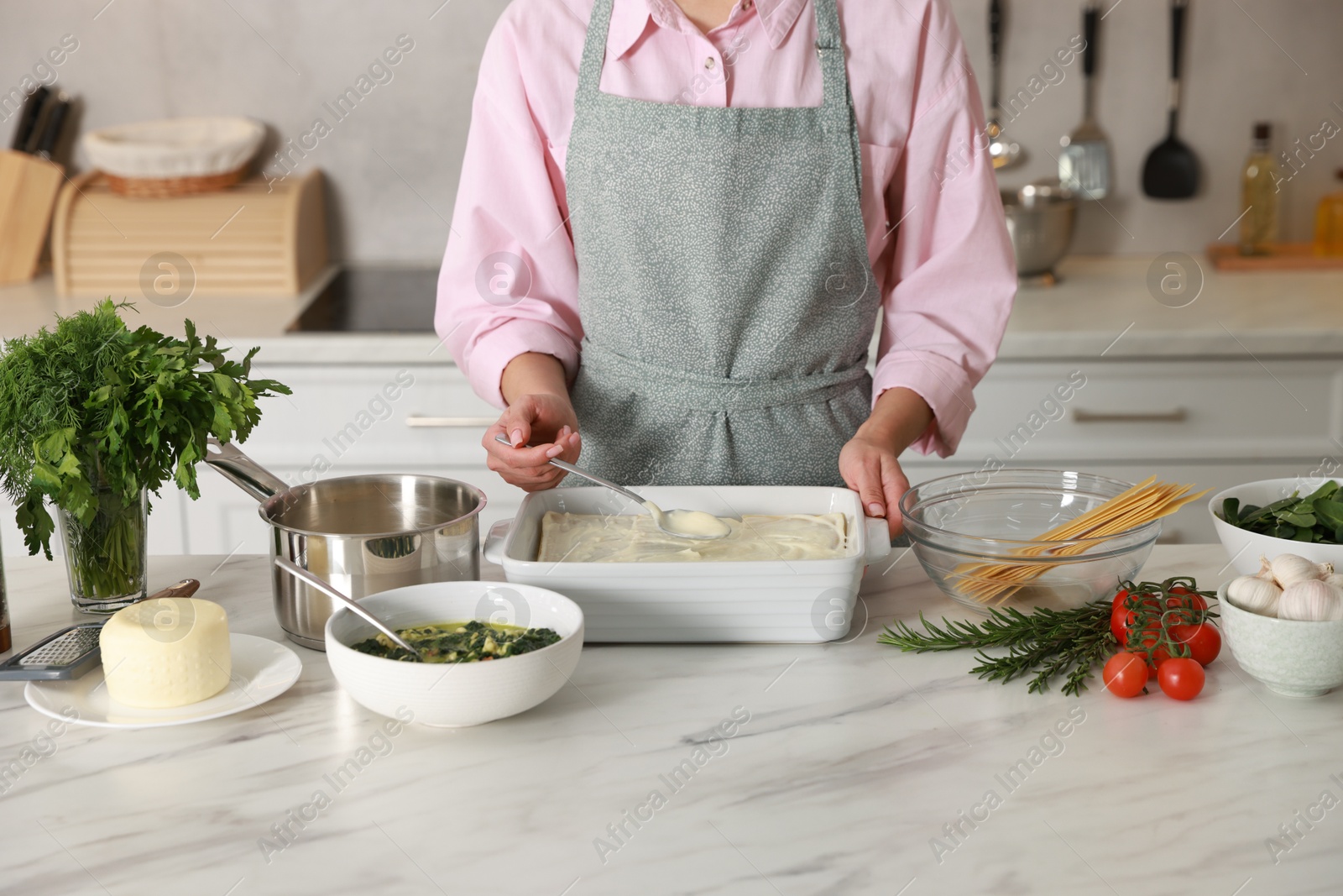 Photo of Woman spreading bechamel sauce onto spinach lasagna at marble table indoors, closeup