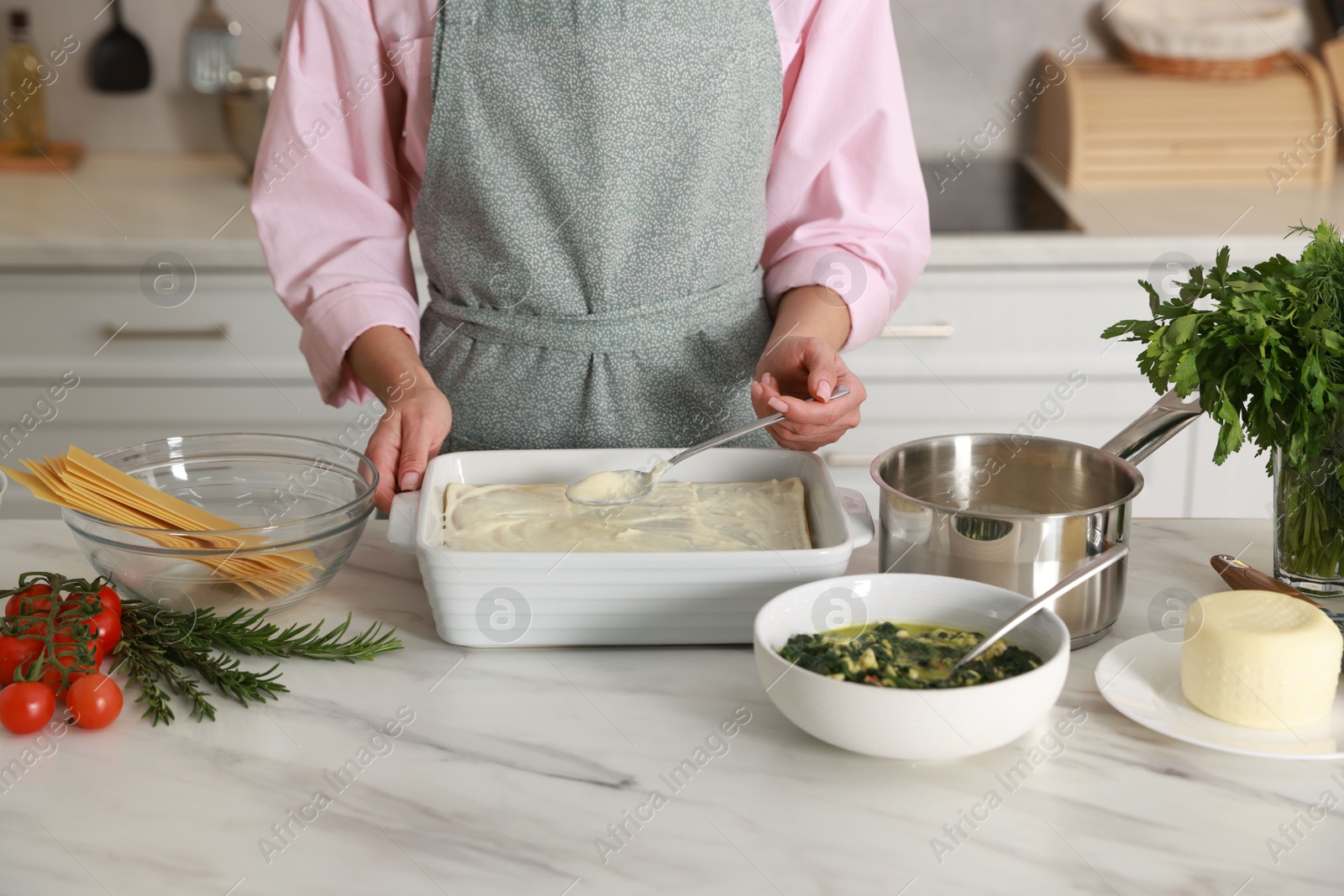 Photo of Woman spreading bechamel sauce onto spinach lasagna at marble table indoors, closeup