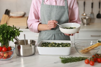 Photo of Woman making spinach lasagna at marble table in kitchen, closeup