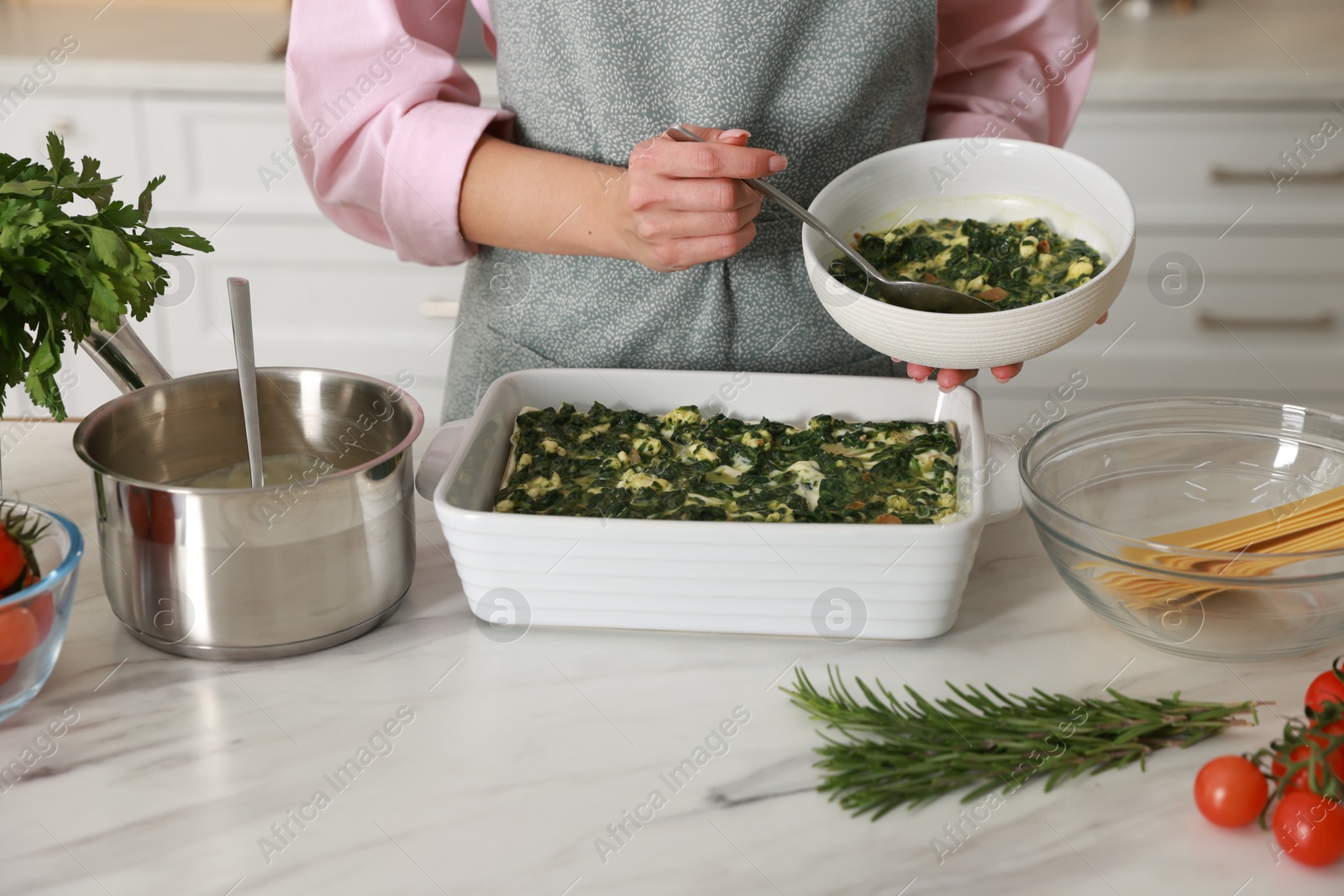 Photo of Woman making spinach lasagna at marble table indoors, closeup