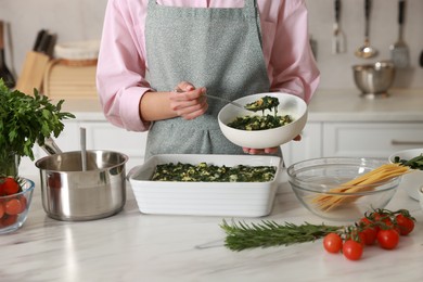 Photo of Woman making spinach lasagna at marble table in kitchen, closeup