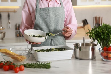 Photo of Woman making spinach lasagna at marble table in kitchen, closeup