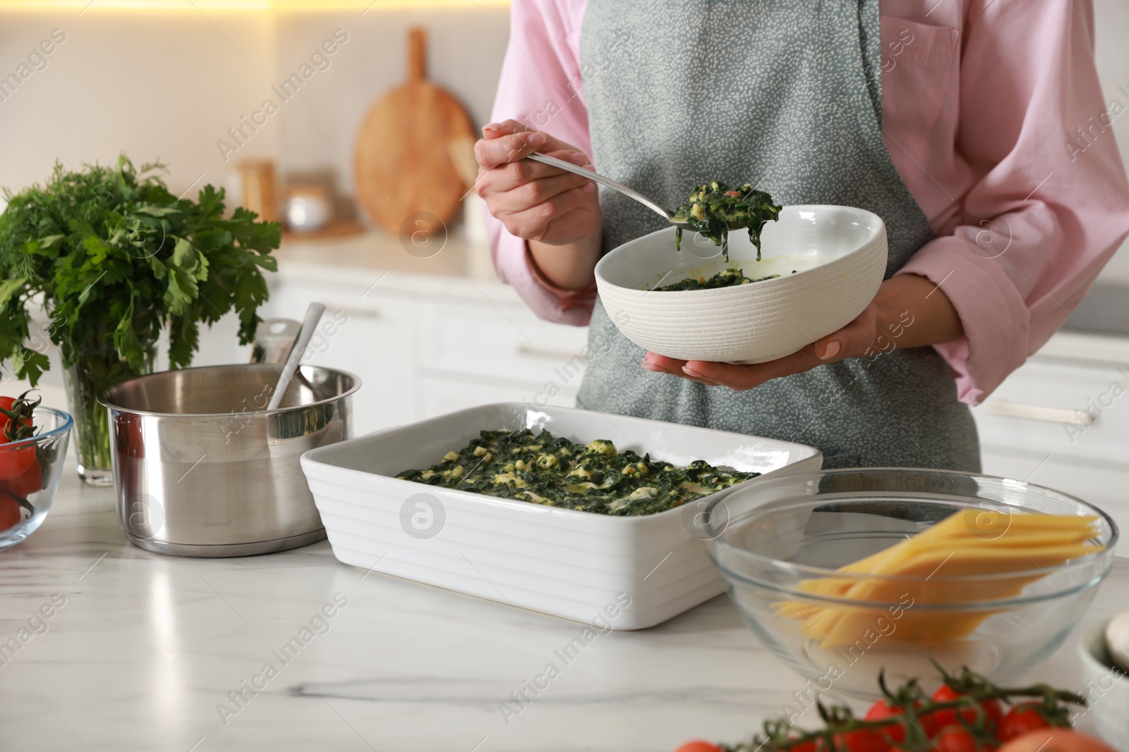 Photo of Woman making spinach lasagna at marble table indoors, closeup