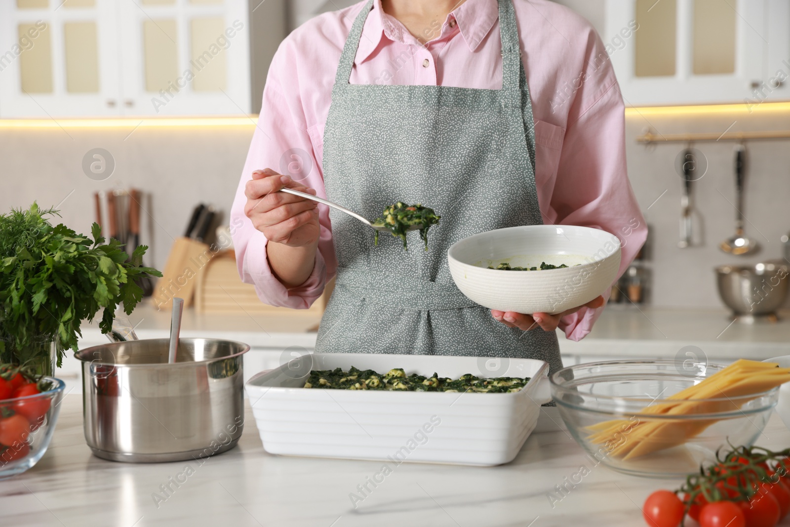 Photo of Woman making spinach lasagna at marble table indoors, closeup