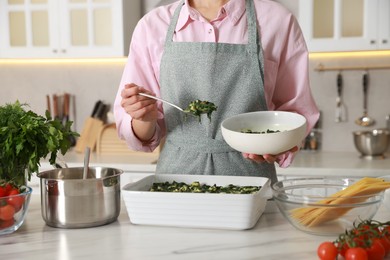 Photo of Woman making spinach lasagna at marble table indoors, closeup