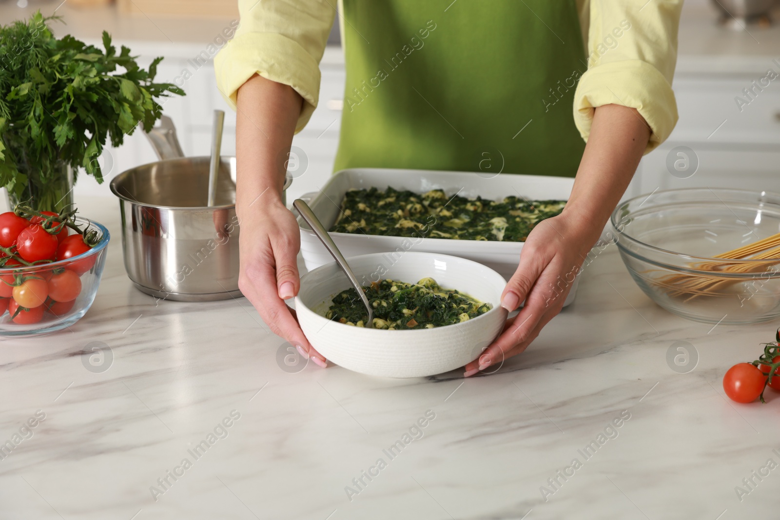 Photo of Woman making spinach lasagna at marble table indoors, closeup