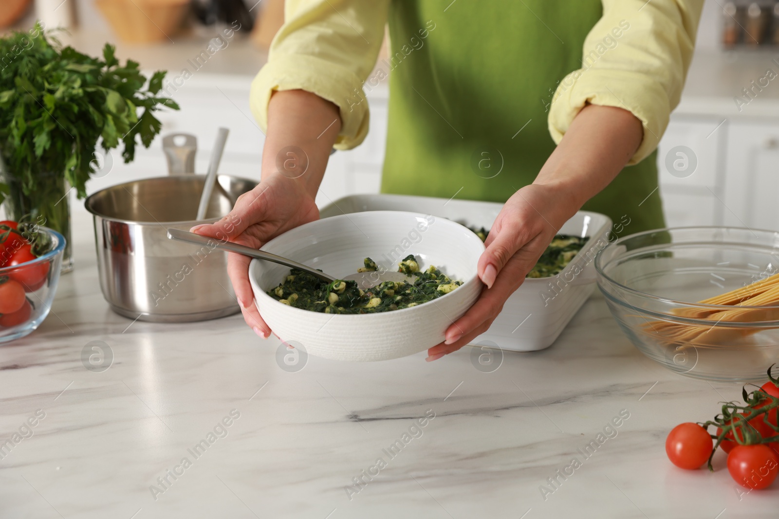 Photo of Woman making spinach lasagna at marble table indoors, closeup