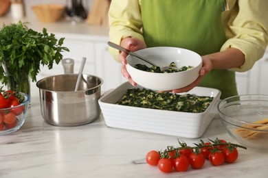 Photo of Woman making spinach lasagna at marble table indoors, closeup