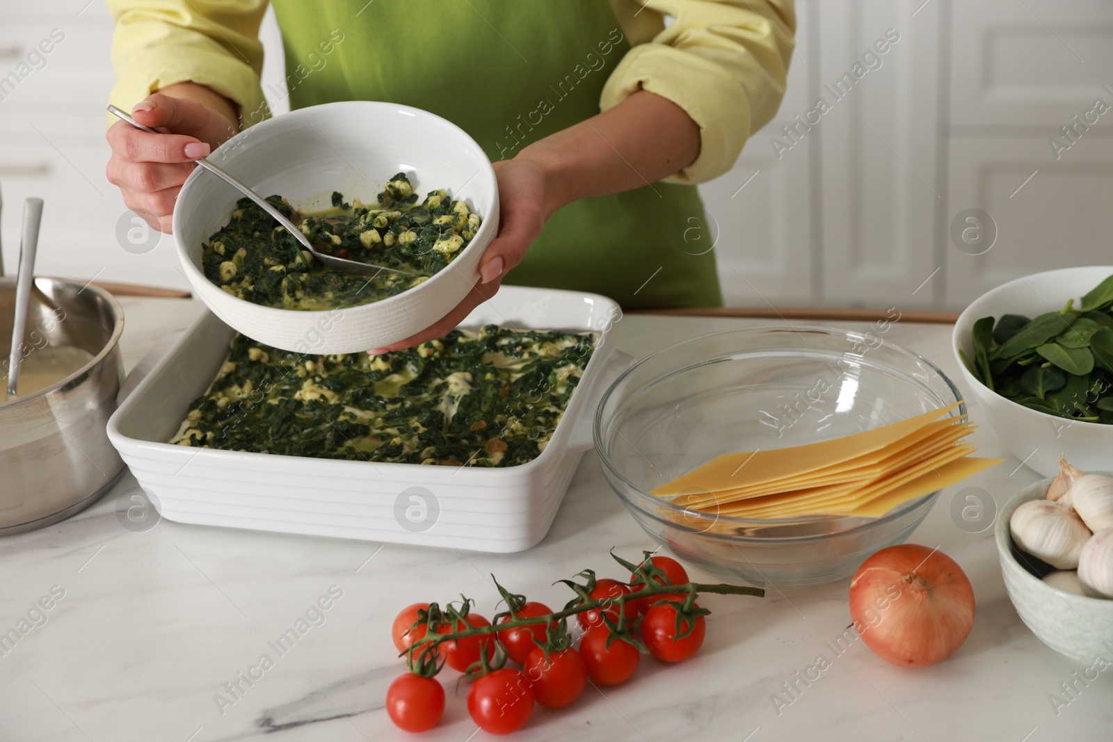 Photo of Woman making spinach lasagna at marble table indoors, closeup