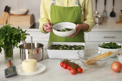 Photo of Woman making spinach lasagna at marble table in kitchen, closeup