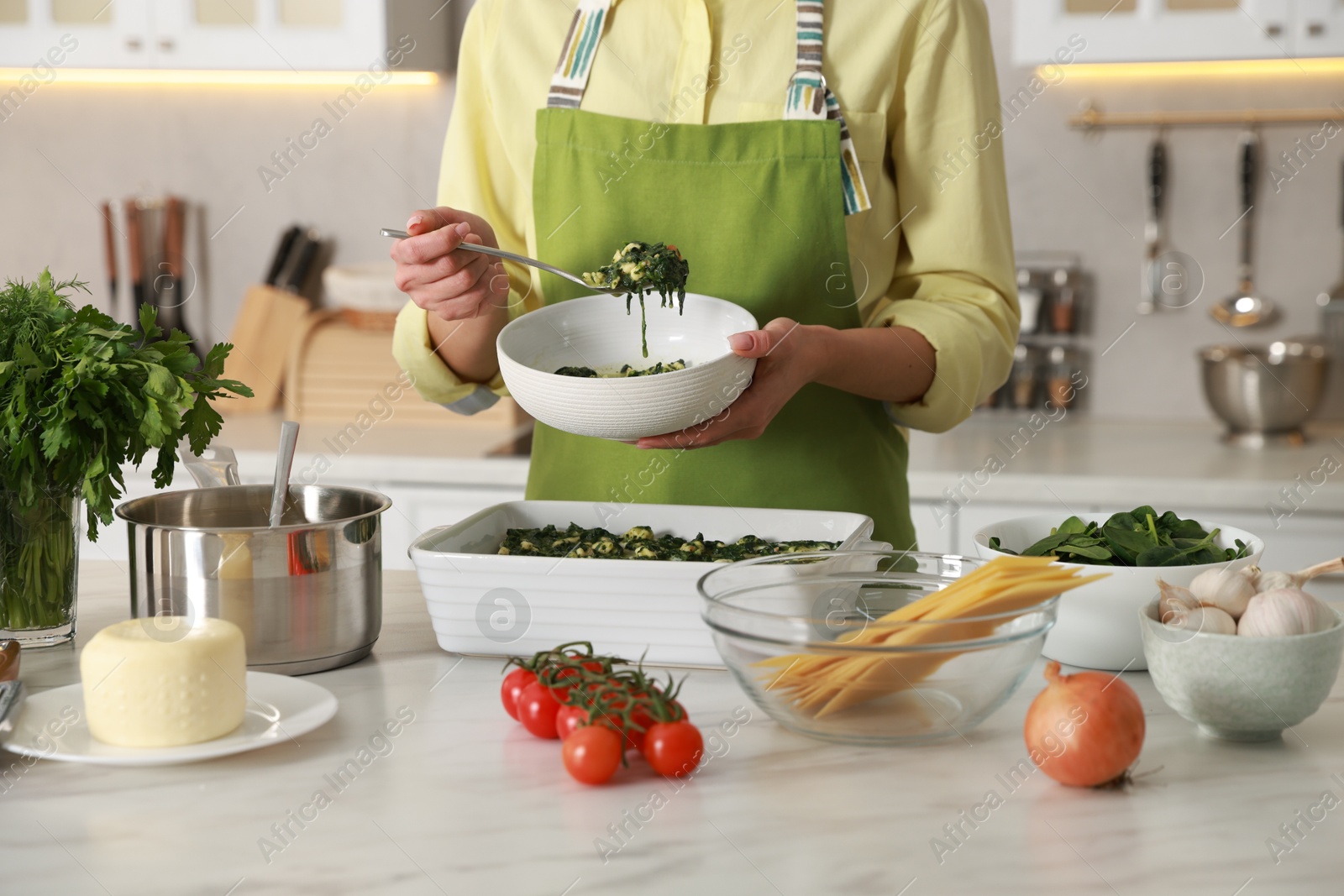 Photo of Woman making spinach lasagna at marble table in kitchen, closeup