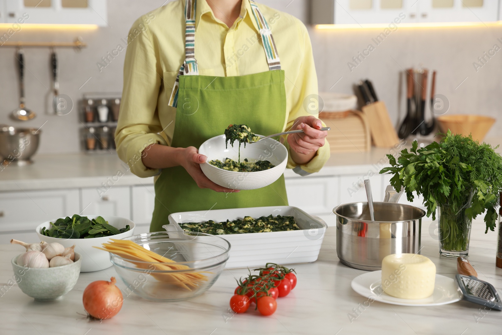 Photo of Woman making spinach lasagna at marble table in kitchen, closeup