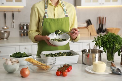 Photo of Woman making spinach lasagna at marble table in kitchen, closeup