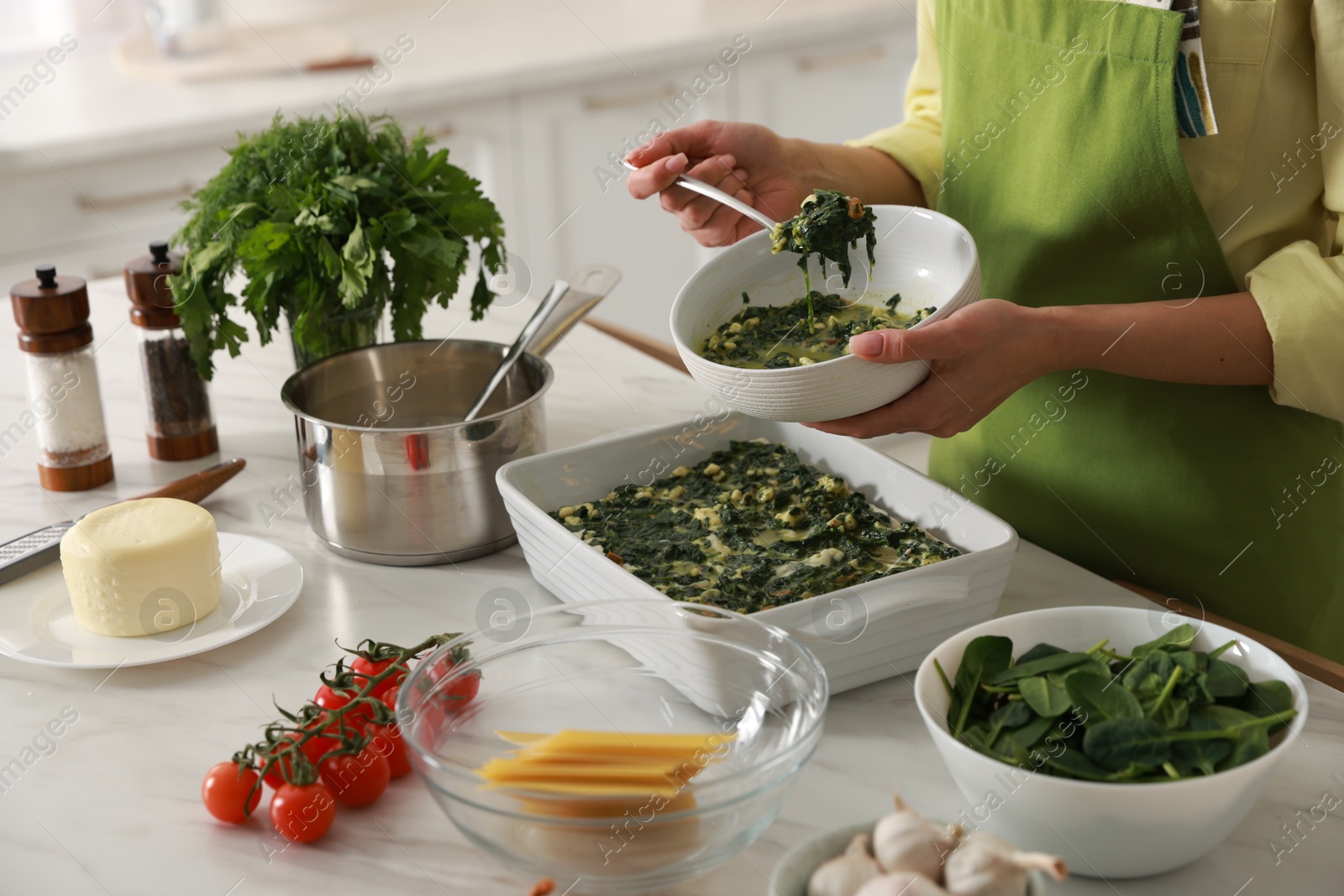 Photo of Woman making spinach lasagna at marble table indoors, closeup