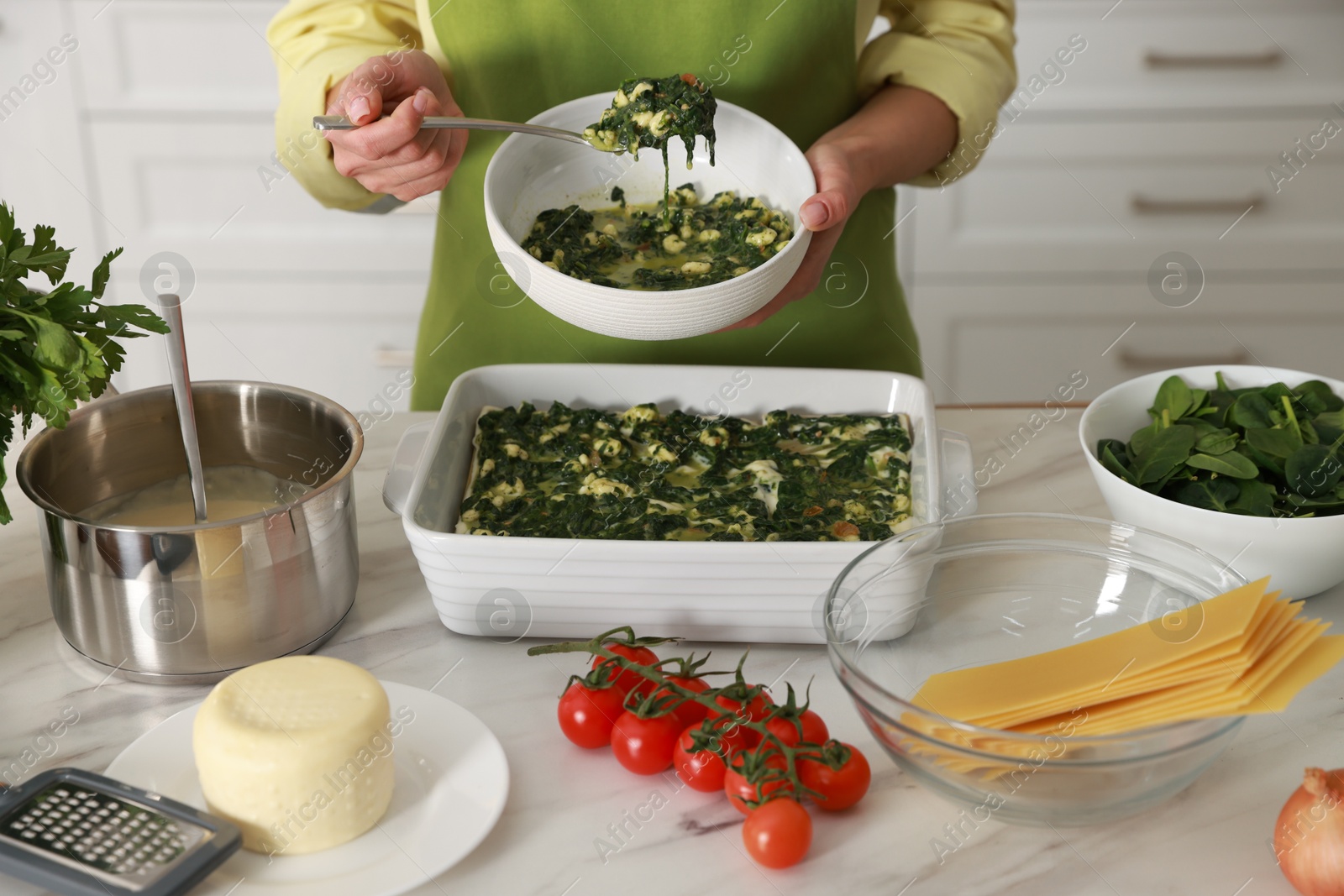 Photo of Woman making spinach lasagna at marble table indoors, closeup