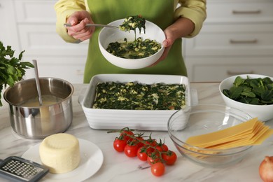 Photo of Woman making spinach lasagna at marble table indoors, closeup