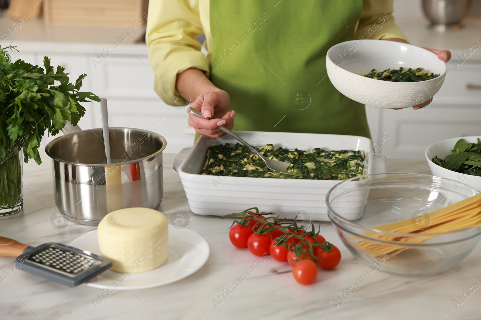 Photo of Woman making spinach lasagna at marble table indoors, closeup