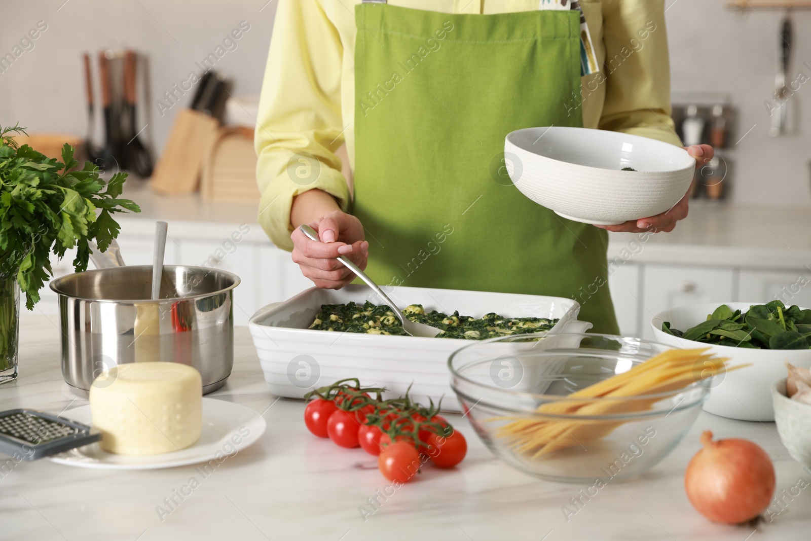 Photo of Woman making spinach lasagna at marble table indoors, closeup