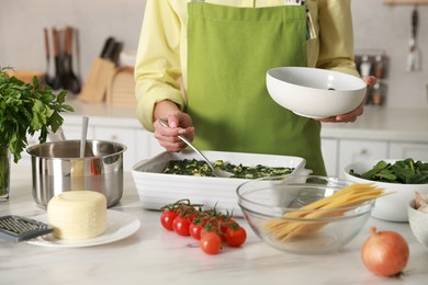 Photo of Woman making spinach lasagna at marble table indoors, closeup