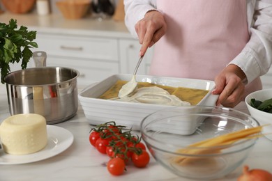 Photo of Woman spreading bechamel sauce onto spinach lasagna at marble table indoors, closeup