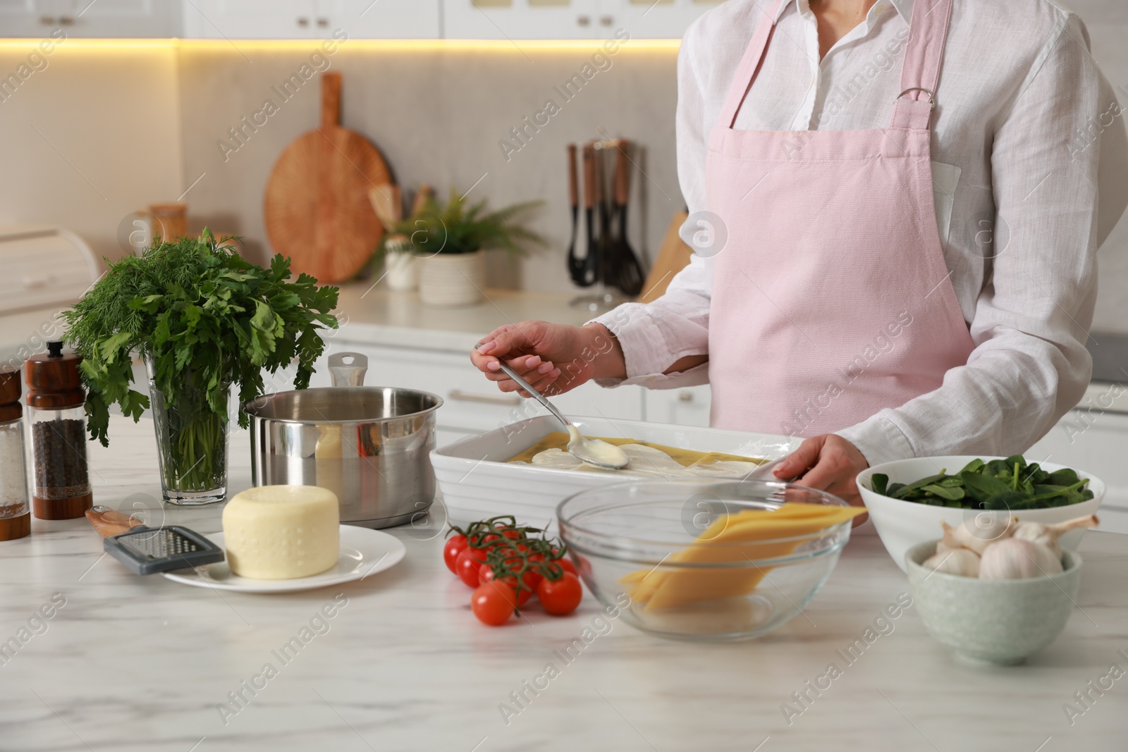 Photo of Woman spreading bechamel sauce onto spinach lasagna at marble table indoors, closeup