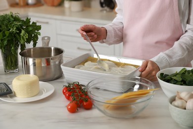 Photo of Woman spreading bechamel sauce onto spinach lasagna at marble table indoors, closeup