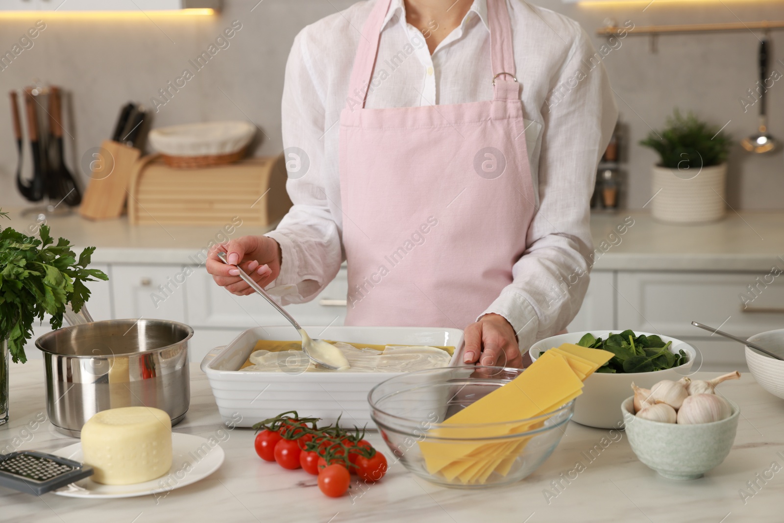 Photo of Woman spreading bechamel sauce onto spinach lasagna at marble table in kitchen, closeup