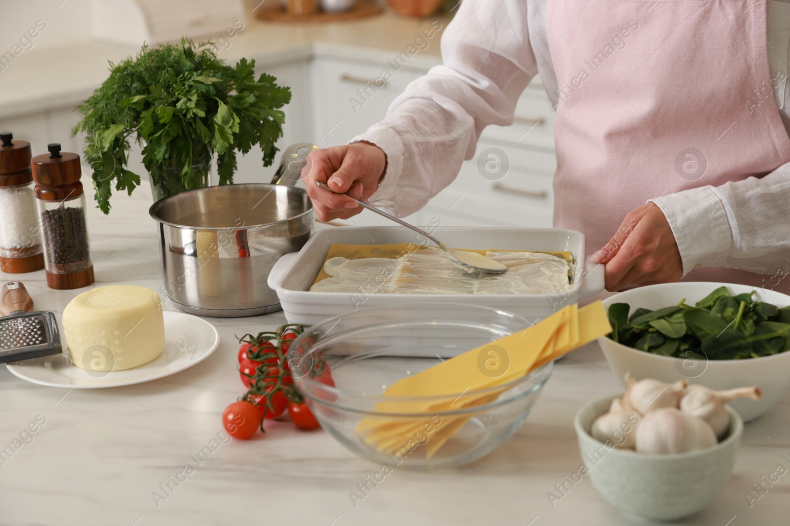 Photo of Woman spreading bechamel sauce onto spinach lasagna at marble table indoors, closeup