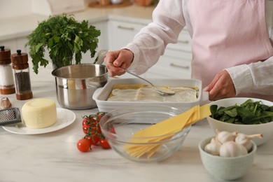 Photo of Woman spreading bechamel sauce onto spinach lasagna at marble table indoors, closeup