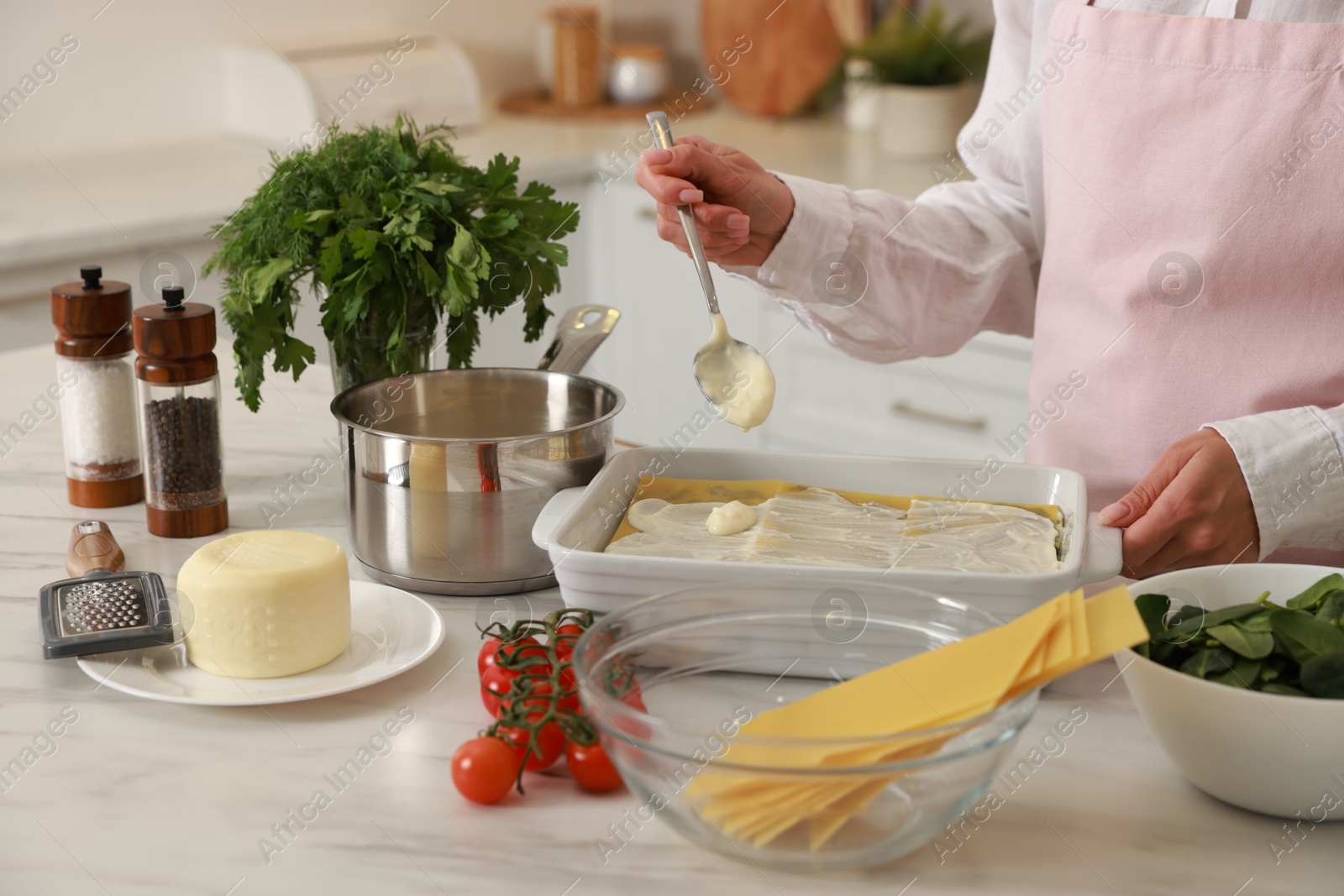 Photo of Woman spreading bechamel sauce onto spinach lasagna at marble table indoors, closeup