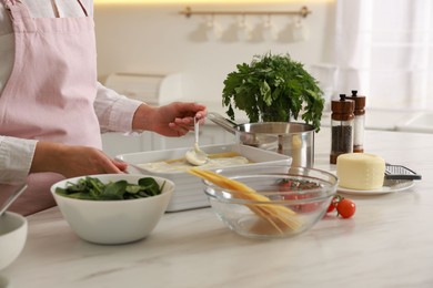 Photo of Woman spreading bechamel sauce onto spinach lasagna at marble table indoors, closeup