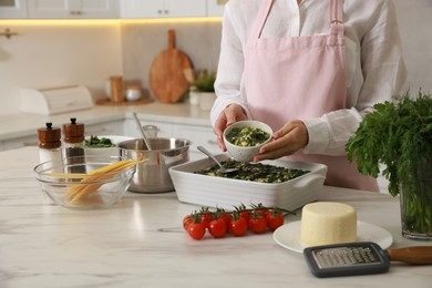 Photo of Woman making spinach lasagna at marble table in kitchen, closeup