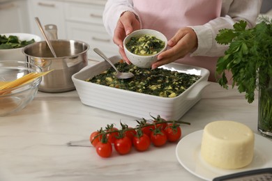 Photo of Woman making spinach lasagna at marble table indoors, closeup